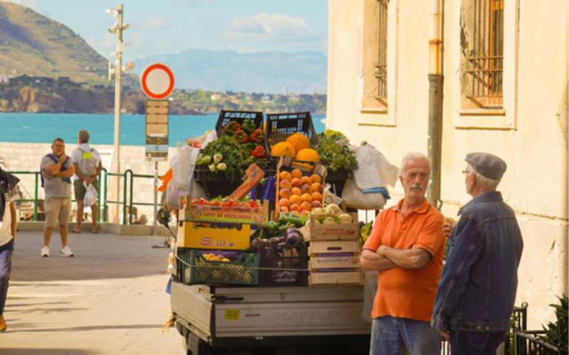 Zwei italienische Männer vor einem Lastwagen voller Obst.